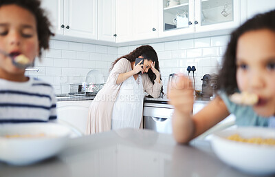 Buy stock photo Shot of a woman looking very stressed talking on cellphone while her kids have breakfast at home