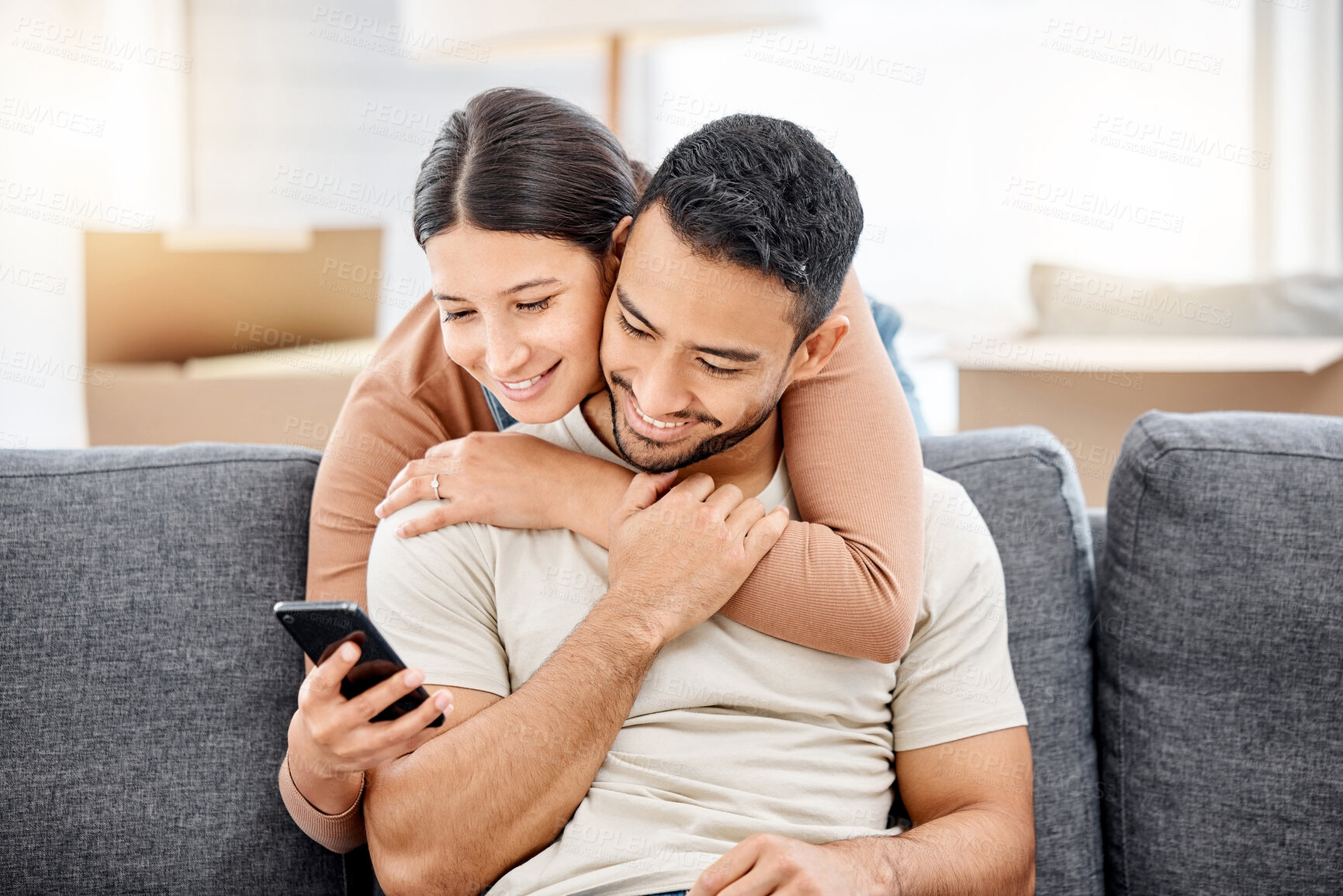 Buy stock photo Couple, hug and happy with phone on sofa for social media search, online research and bonding in home. People, embrace and smile on couch with smartphone for web browsing, reading post and affection