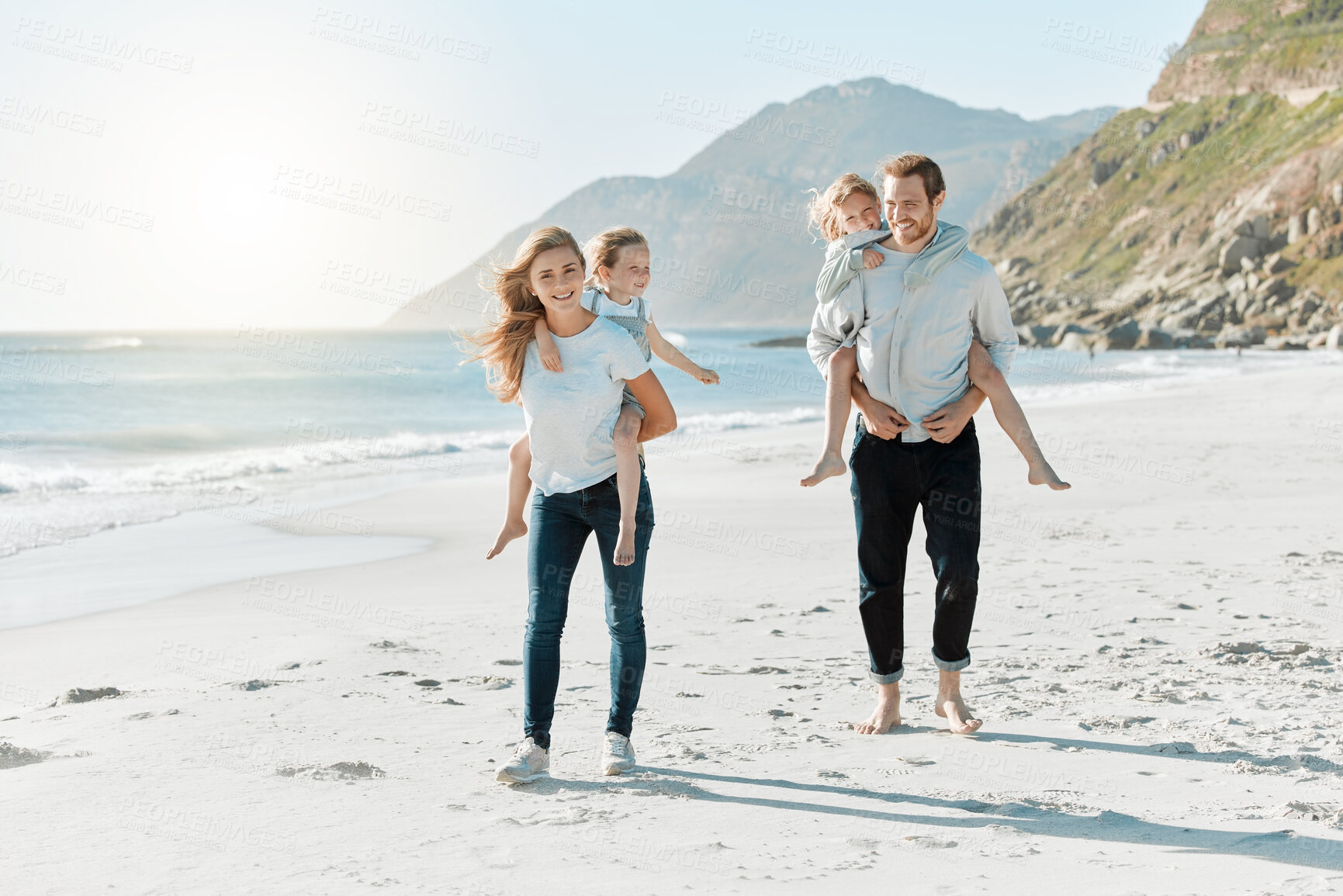 Buy stock photo Shot of a couple carrying their daughters on their backs while at the beach