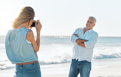 Buy stock photo Shot of a woman taking a picture of her husband while at the beach