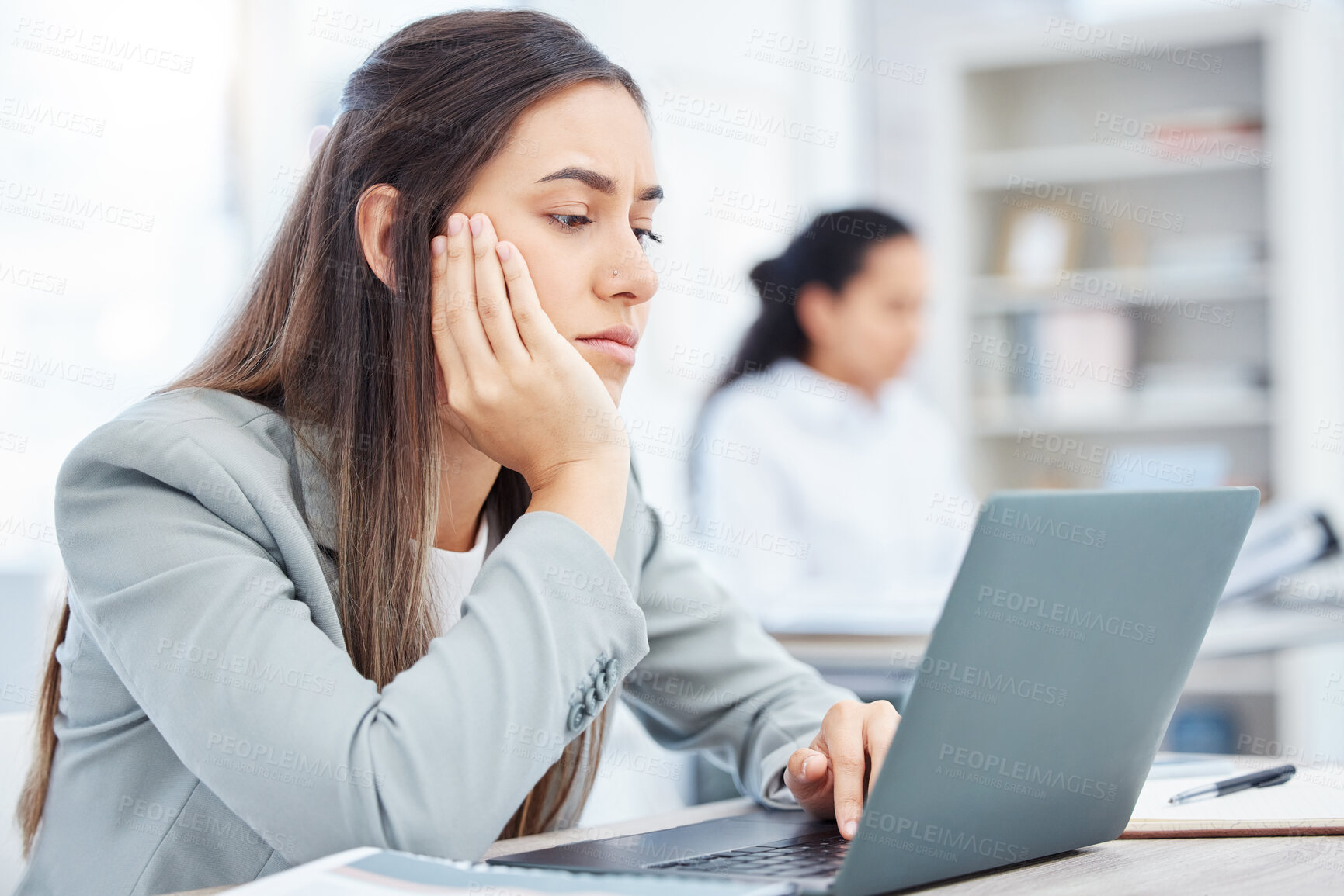 Buy stock photo Shot of a young businesswoman looking bored while using a laptop in an office at work