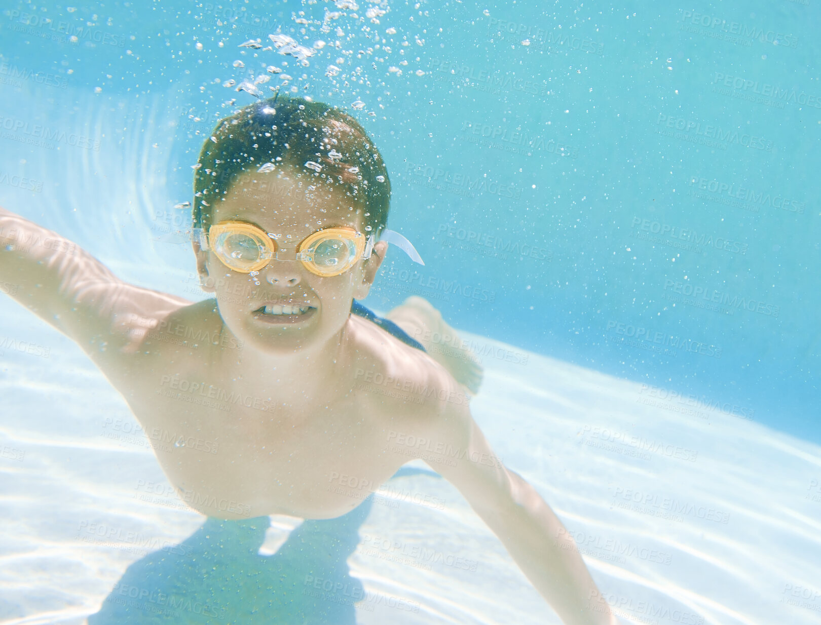 Buy stock photo Shot of a little boy wearing swimming goggles while swimming underwater
