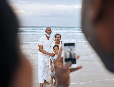 Buy stock photo Cropped shot of an unrecognizable man taking a picture of a mature couple and their grandson at the beach