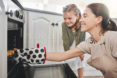 Buy stock photo Shot of a mother and daughter putting a tray of cookies in the oven at home