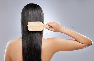 Buy stock photo Shot of a young woman brushing her hair while standing against a grey background