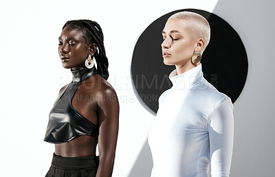 Buy stock photo Shot of two attractive young women posing against a wall with a black circle on it