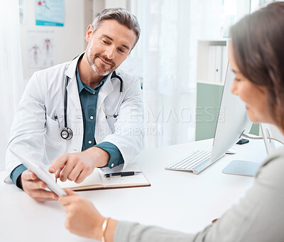 Buy stock photo Shot of a mature doctor using a digital tablet during a consultation with a patient in a medical office