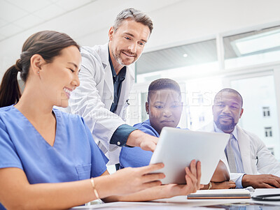 Buy stock photo Shot of a group of young doctors looking at a tablet during a meeting in the hospital boardroom