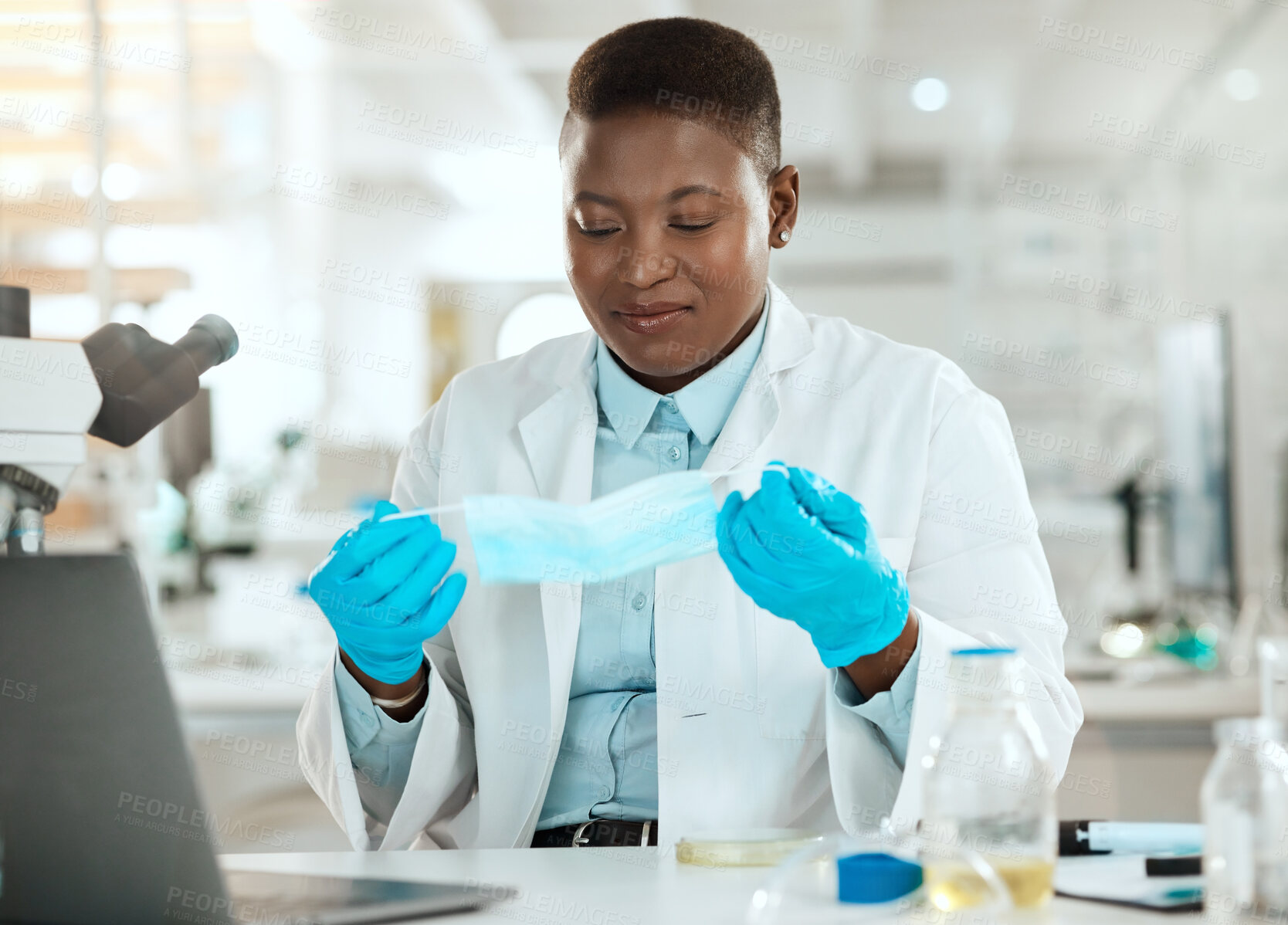 Buy stock photo Shot of an attractive young scientist sitting alone in her laboratory and putting a face mask on