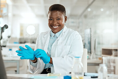 Buy stock photo Shot of an attractive young scientist sitting alone in her laboratory and putting surgical gloves on
