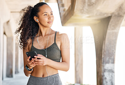 Buy stock photo Shot of an attractive young woman standing in city and using her cellphone to listen to music during her workout