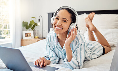 Buy stock photo Shot of a young woman listening to music while using a laptop on her bed at home