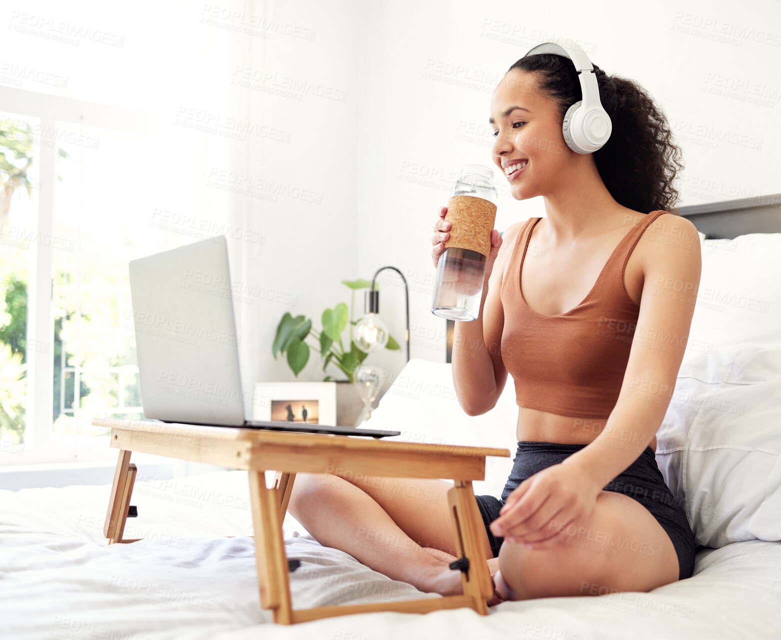 Buy stock photo Shot of a young woman using a laptop while sitting on her bed at home