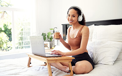 Buy stock photo Shot of a young woman using a laptop while sitting on her bed at home