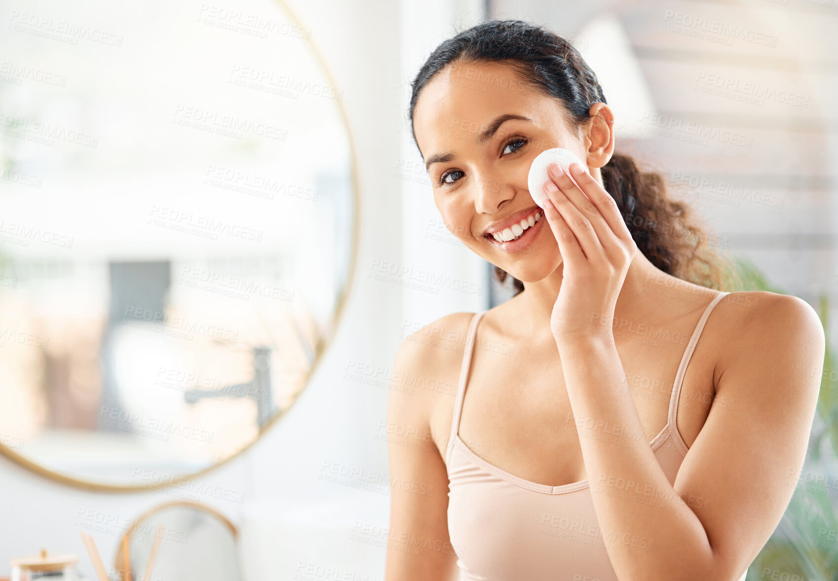 Buy stock photo Shot of a young woman using a cotton pad to clean her face in a bathroom at home