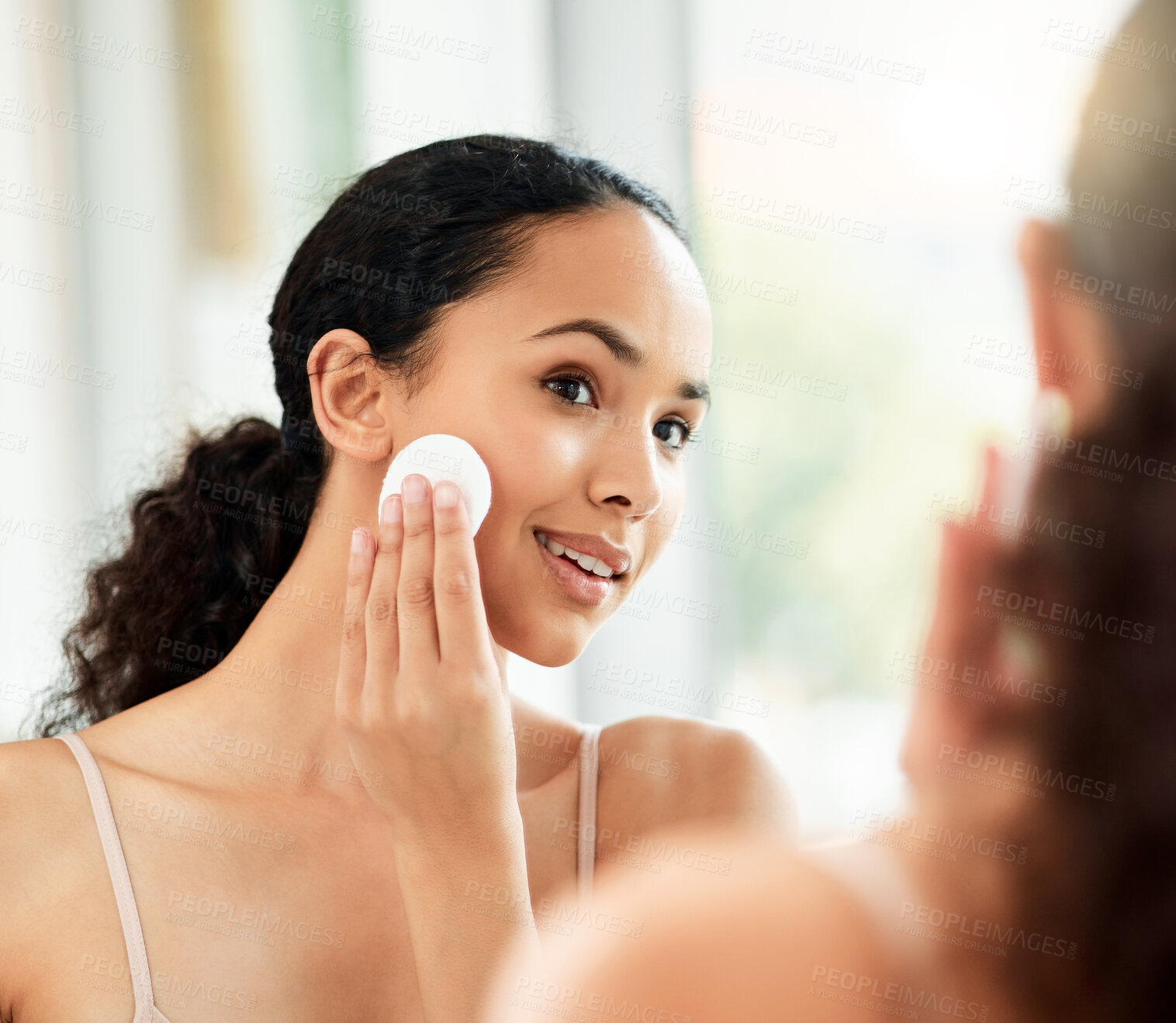 Buy stock photo Shot of a young woman using a cotton pad to clean her face in a bathroom at home