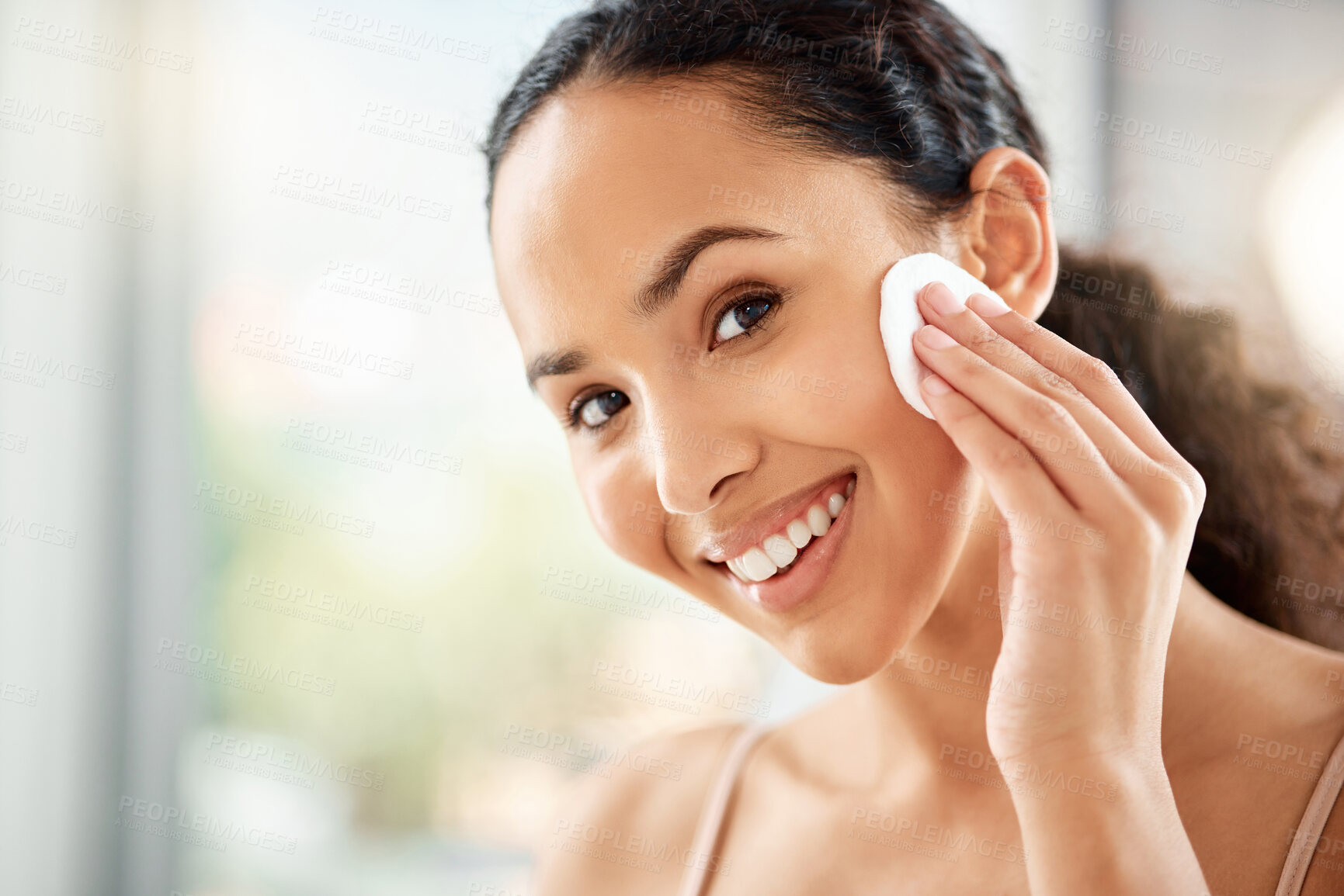 Buy stock photo Shot of a young woman using a cotton pad to clean her face in a bathroom at home