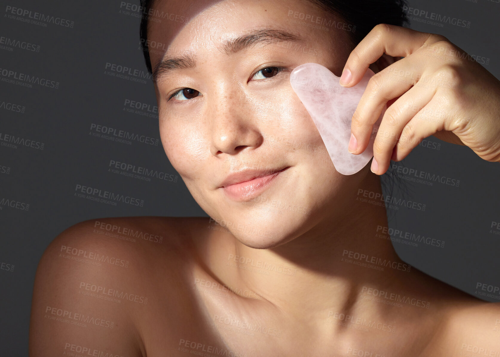 Buy stock photo Studio shot of a beautiful young woman using a scraping tool on her face