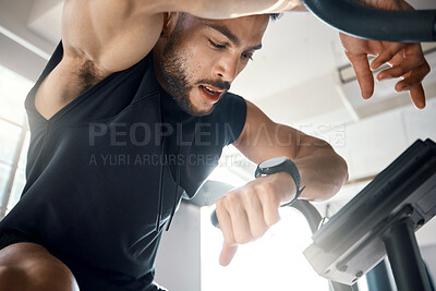 Buy stock photo Low angle shot of a sporty young man checking his watch while exercising in a gym