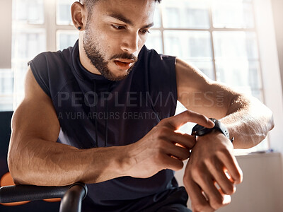 Buy stock photo Shot of a sporty young man checking his watch while exercising in a gym