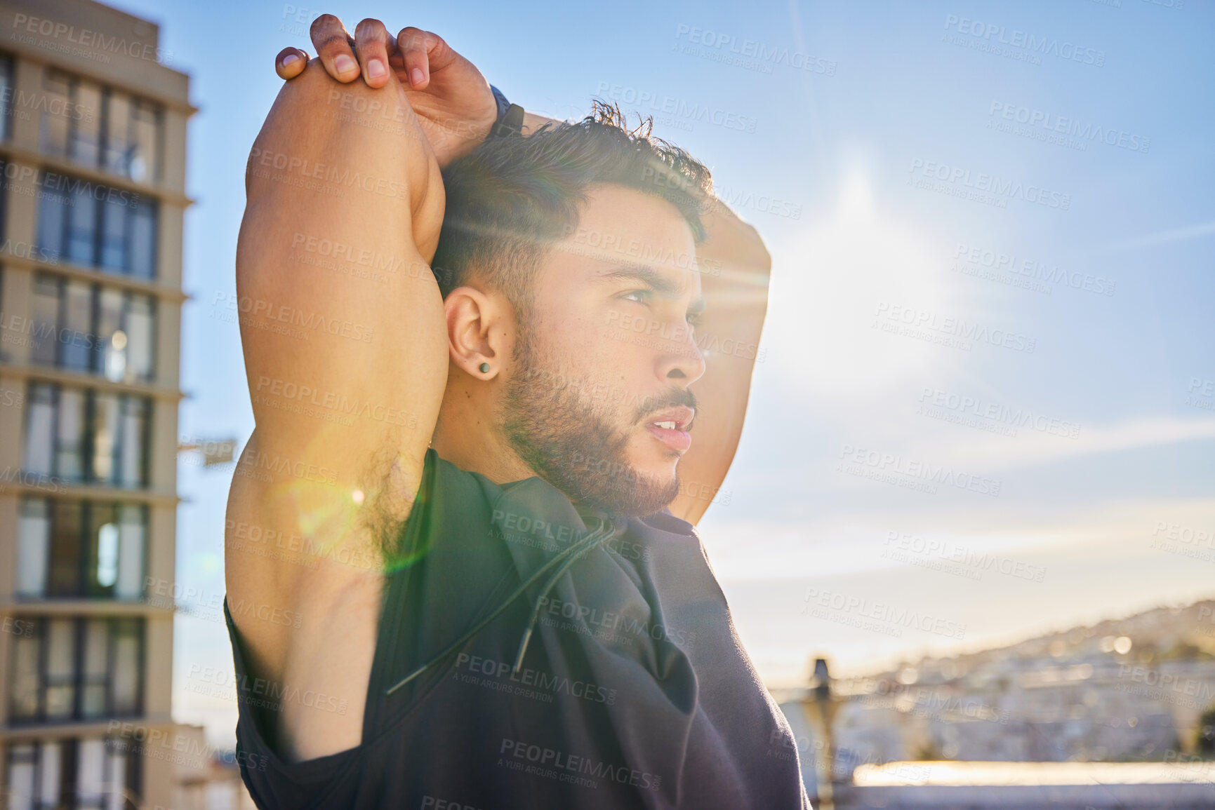 Buy stock photo Shot of a sporty young man stretching while on a rooftop