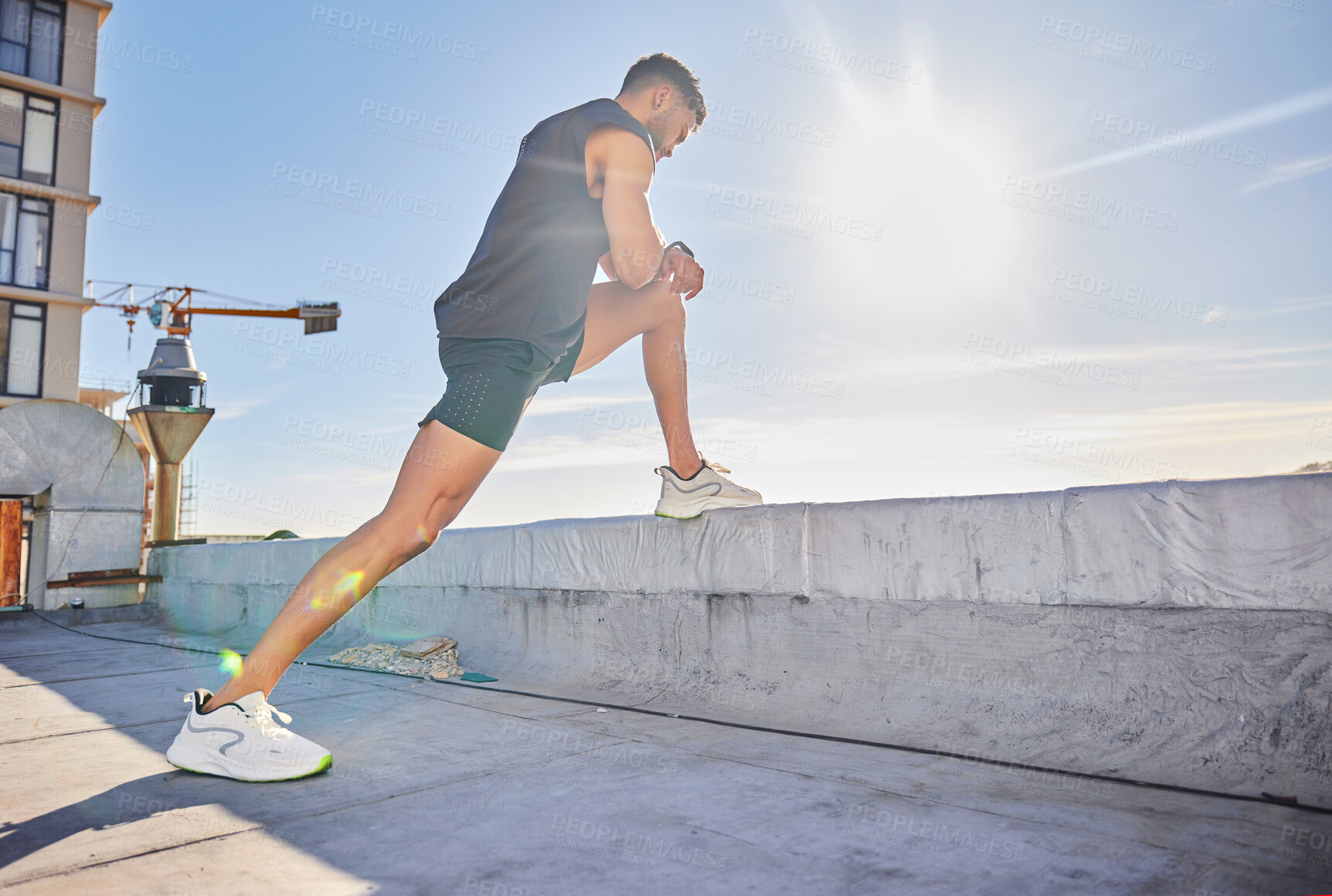 Buy stock photo Shot of a sporty young man stretching while on a rooftop