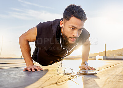 Buy stock photo Shot of a sporty young man wearing earphones while doing push-ups, on a rooftop