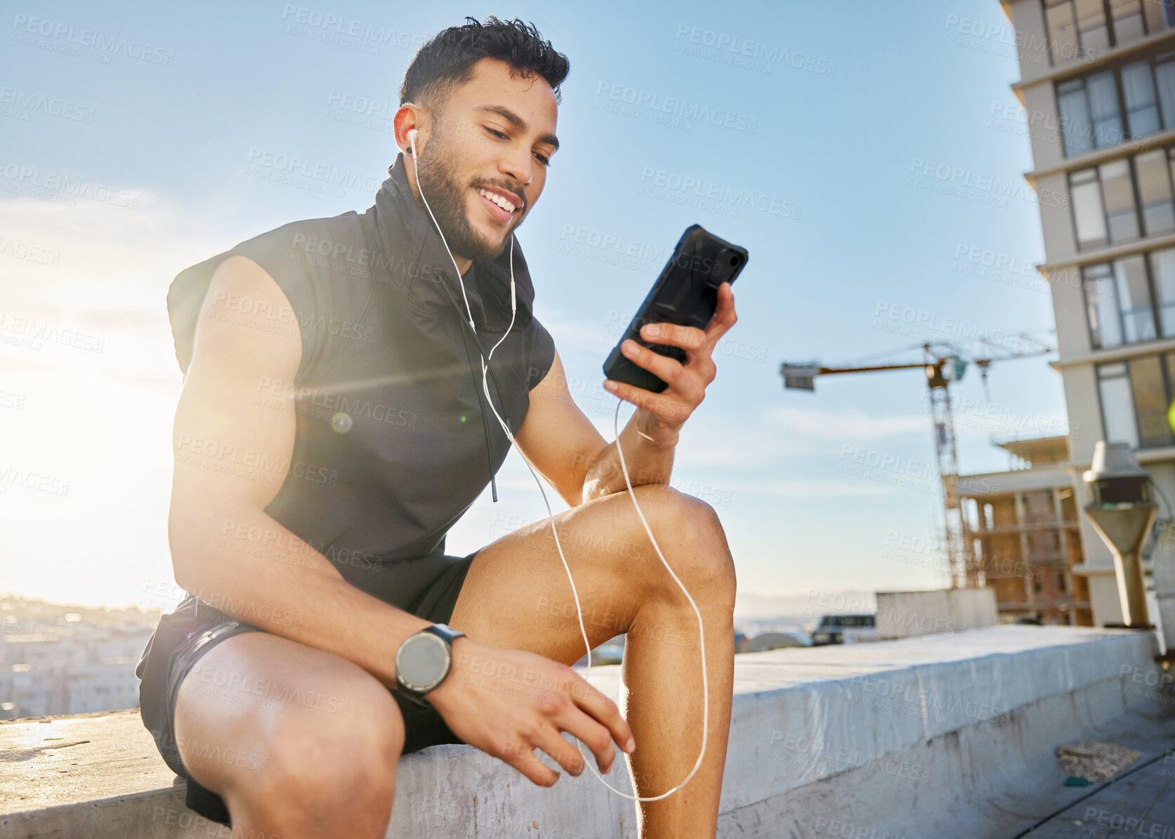 Buy stock photo Phone, fitness and earphones with man in city for workout playlist, health app and communication. Training podcast, music and wellness with person on rooftop for social media, contact and audio