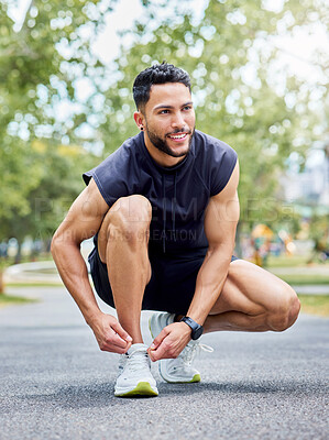 Buy stock photo Shot of a sporty young man tying his laces while exercising outdoors