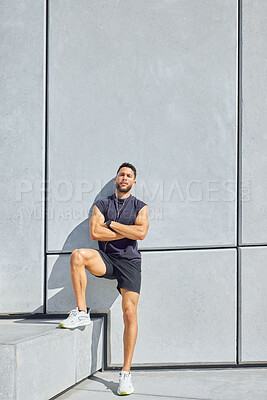 Buy stock photo Portrait of a sporty young man listening to music and standing with his arms crossed while exercising outdoors