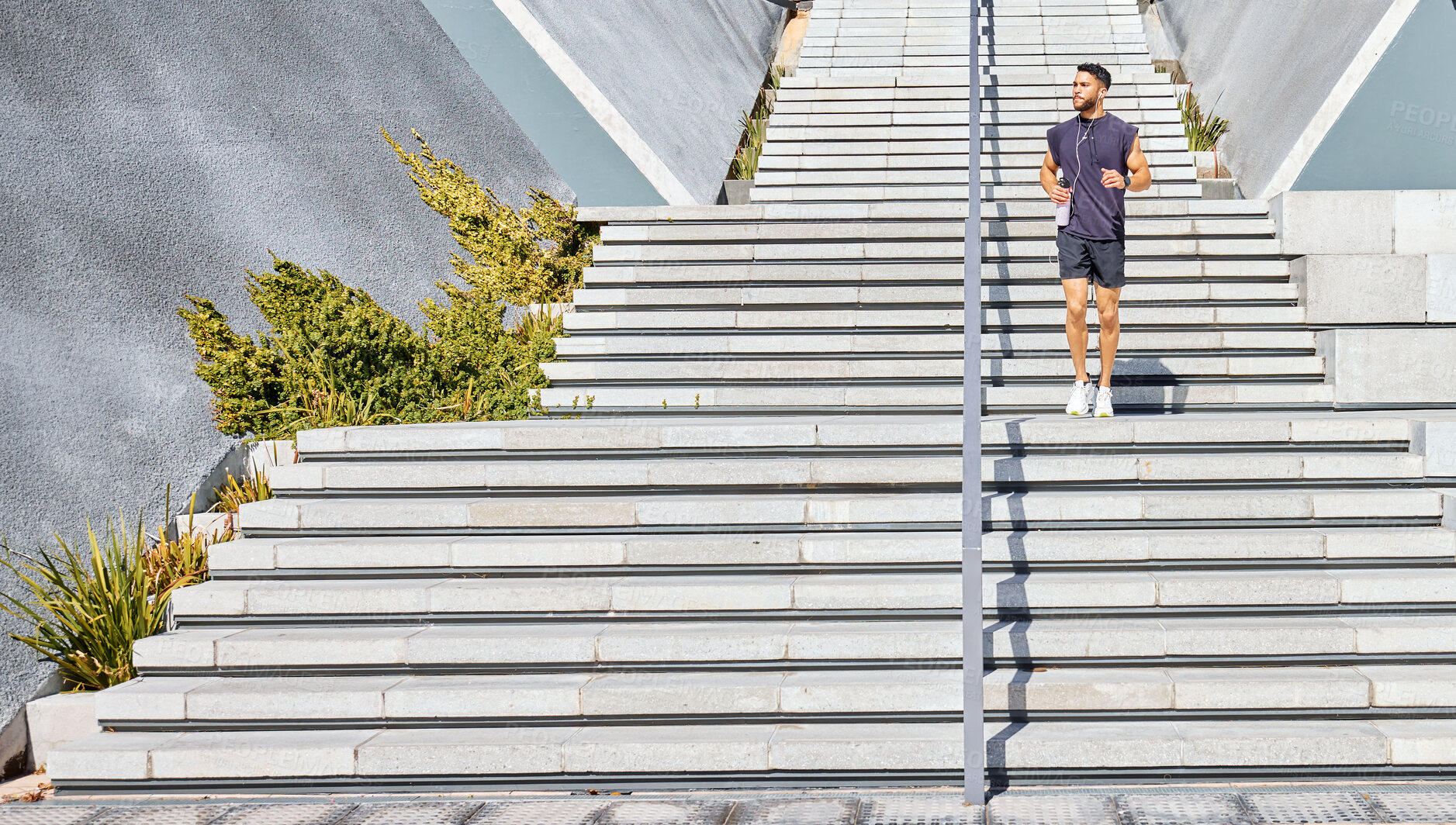 Buy stock photo Shot of a sporty young man listening to music and carrying a water bottle while exercising outdoors