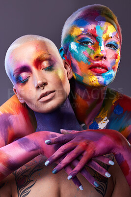 Buy stock photo Studio shot of two young women posing with multi-coloured paint on her face