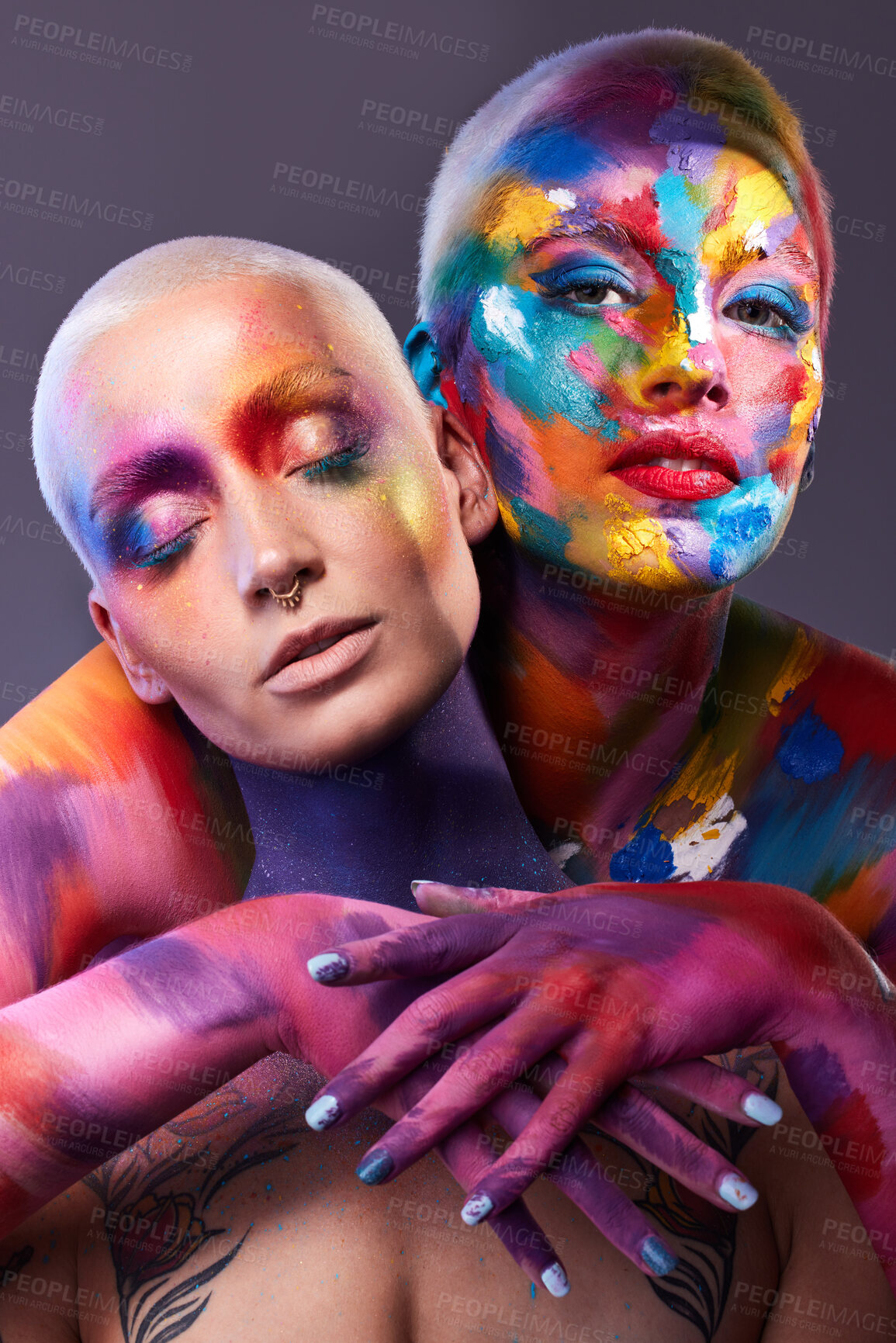 Buy stock photo Studio shot of two young women posing with multi-coloured paint on her face