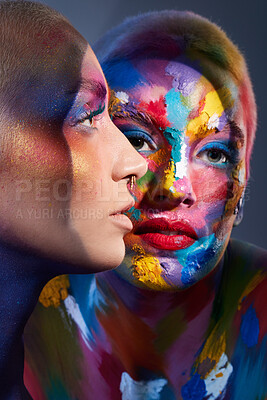 Buy stock photo Studio shot of two young women posing with multi-coloured paint on her face