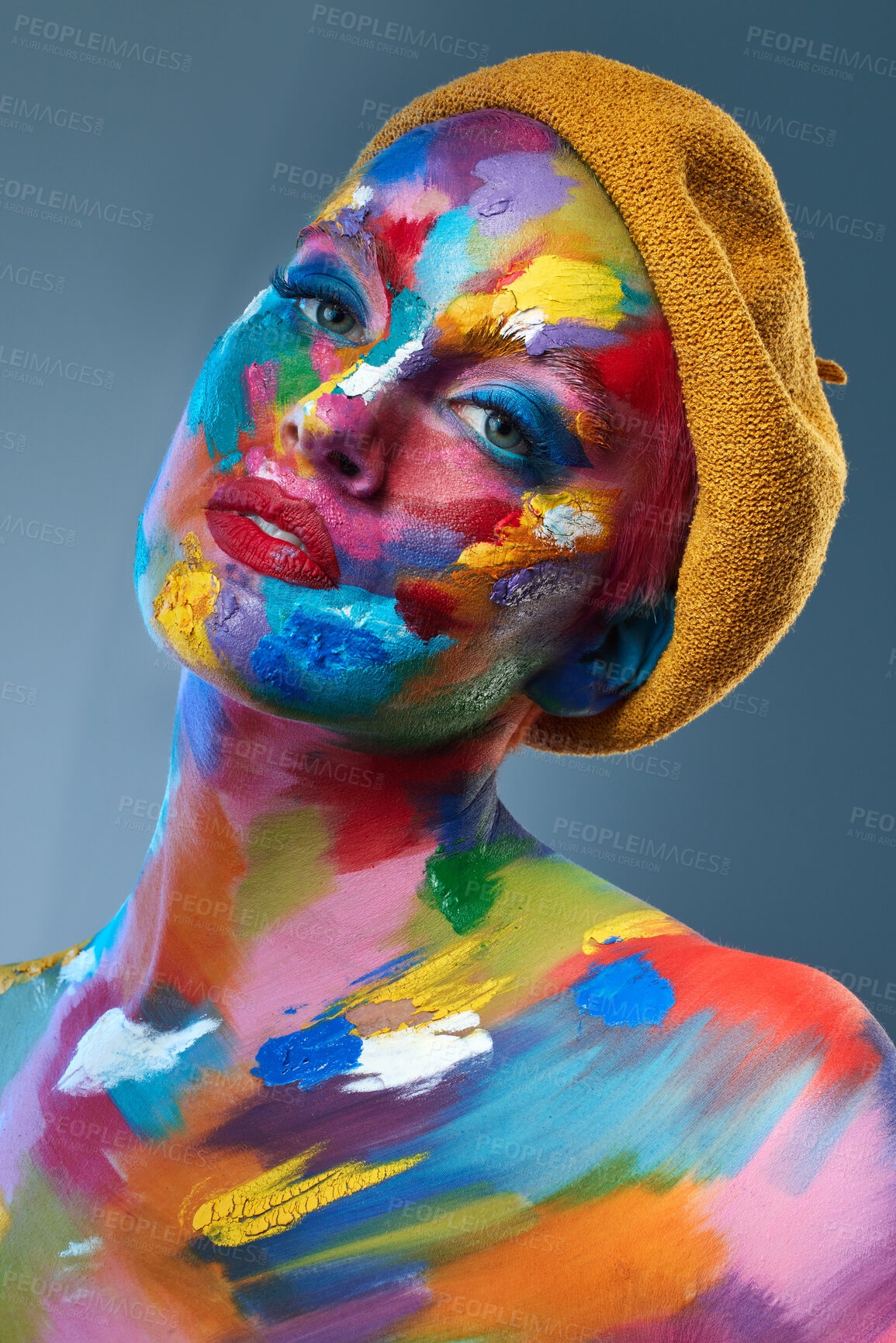 Buy stock photo Studio shot of a young woman posing with multi-coloured paint on her face and a french hat on her head