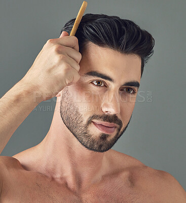 Buy stock photo Shot of a handsome young man combing his hair while standing against a grey background