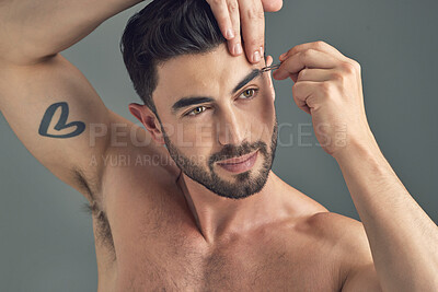 Buy stock photo Shot of a handsome young man tweezing his eyebrows