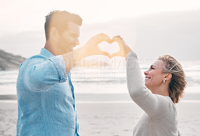 Buy stock photo Beach, happy couple and heart hands for love, support and care on holiday outdoor. Romance, man and woman with sign at ocean for healthy relationship, connection and commitment in summer with flare