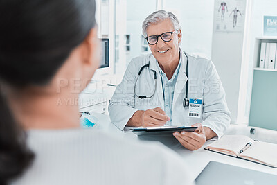 Buy stock photo Shot of a mature doctor sitting with his patient and holding a clipboard during a consultation in his clinic