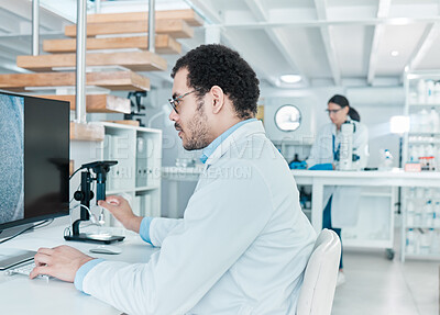 Buy stock photo Shot of a young scientist using a digital microscope while working on a computer in a lab