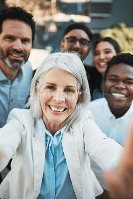 Buy stock photo Shot of a mature businesswoman standing outside with her colleagues and taking selfies