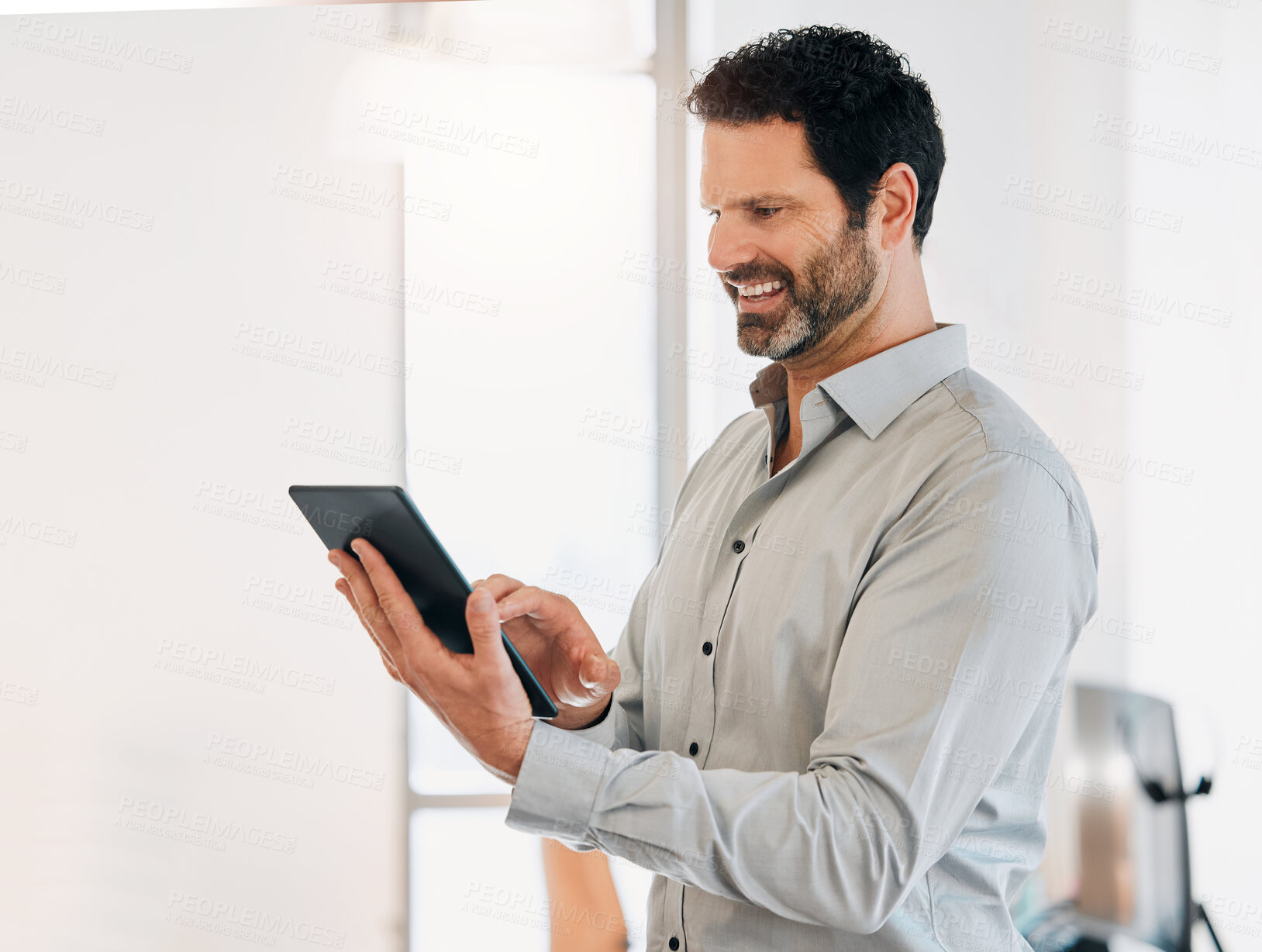 Buy stock photo Shot of a mature businessman standing alone in the office and using a digital tablet