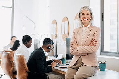 Buy stock photo Shot of a mature businesswoman sitting in the office with her arms folded while her team work behind her
