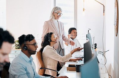 Buy stock photo Shot of a mature businesswoman standing and talking to two young agents while they uses their computers
