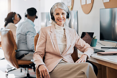 Buy stock photo Shot of a mature businesswoman sitting in the office and wearing a headset while her colleagues work behind her