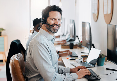 Buy stock photo Shot of a mature agent sitting in the office and using his computer while his colleagues work behind him
