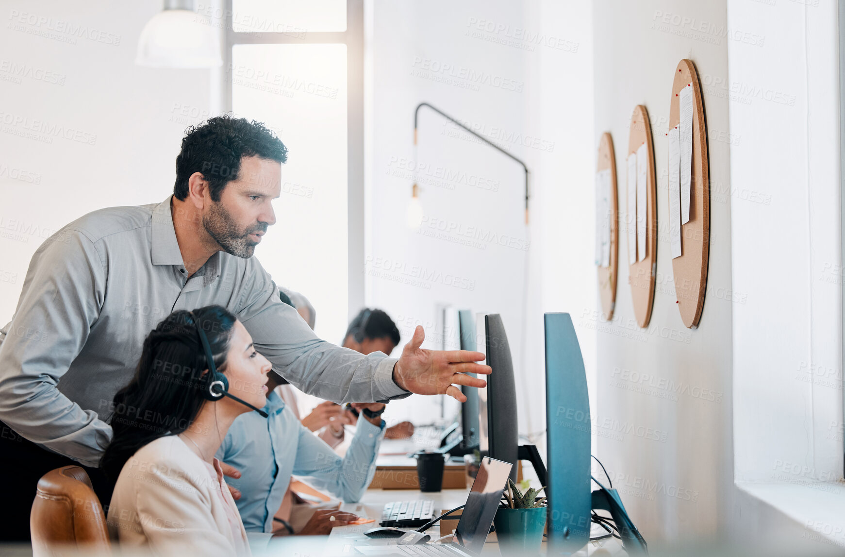 Buy stock photo Shot of a mature businessman standing and talking to a young agent while she uses her computer