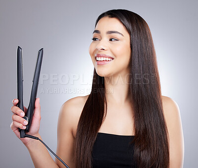 Buy stock photo Studio shot of an attractive young woman using a flat iron to straighten her hair against a grey background