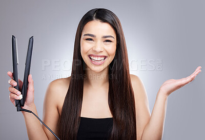 Buy stock photo Studio portrait of an attractive young woman using a flat iron to straighten her hair against a grey background
