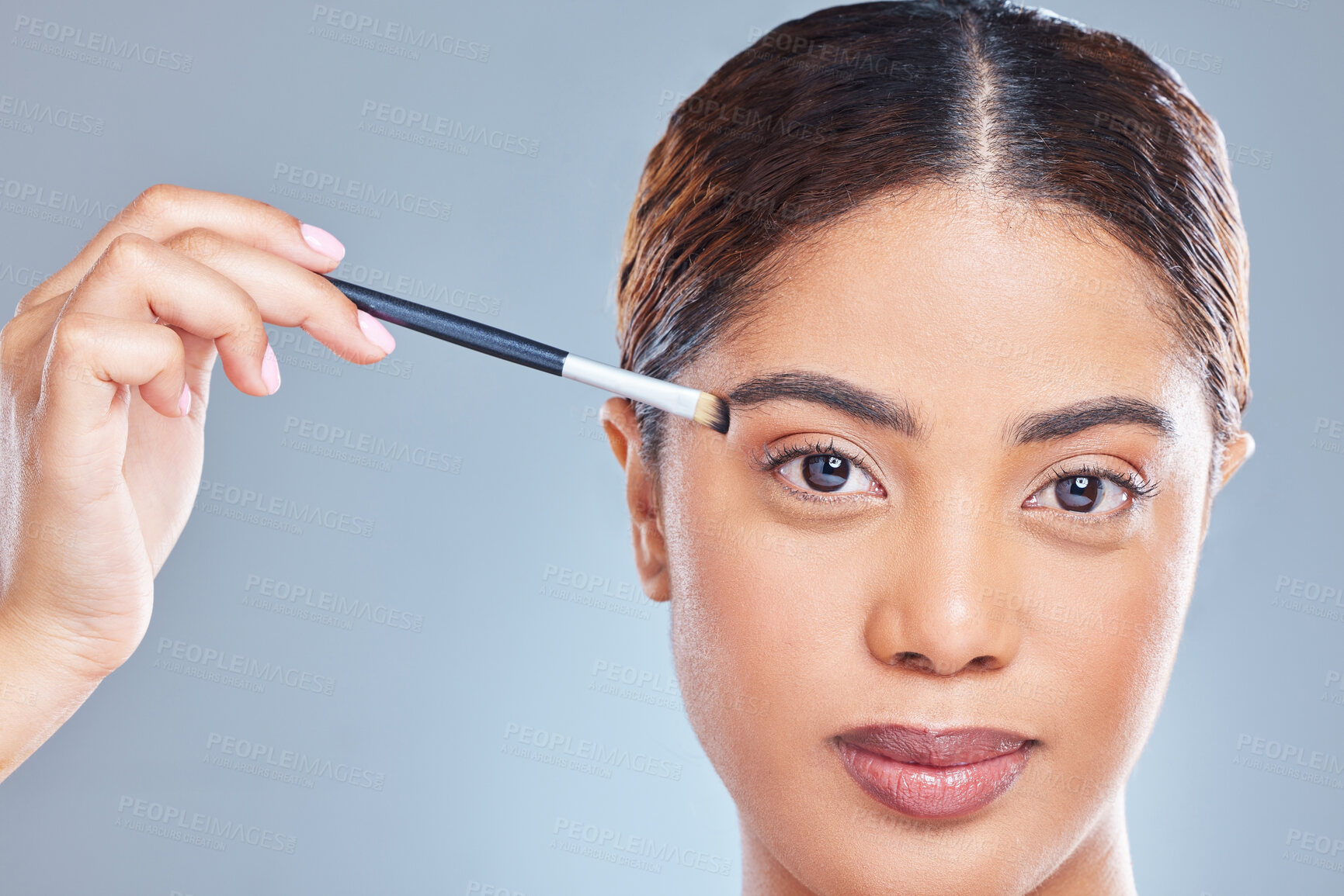 Buy stock photo Shot of a young woman applying makeup to her face against a grey background